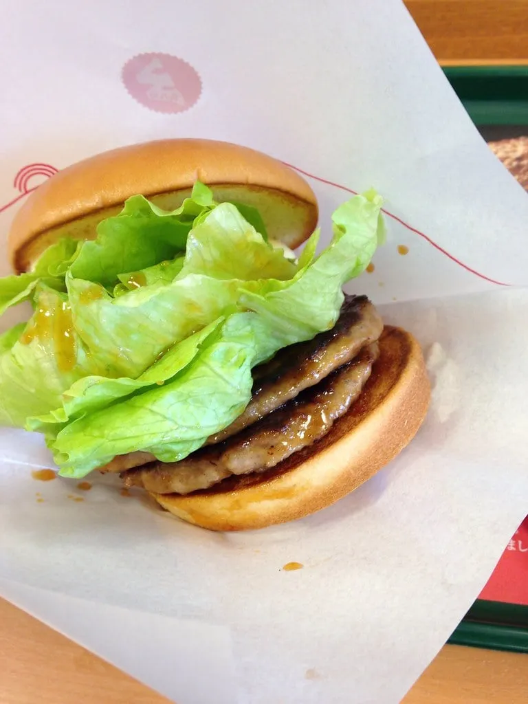 Teriyaki burger de MOS Burger à deux steaks laqués de sauce teriyaki, mayonnaise et laitue, sur son papier d’emballage