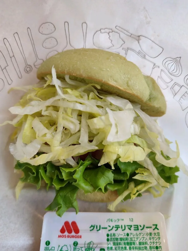 Green Burger Teriyaki de MOS Burger, burger vegan au pain vert, laitue émincée et en feuilles, avec son sachet de sauce Green Teri-Mayo