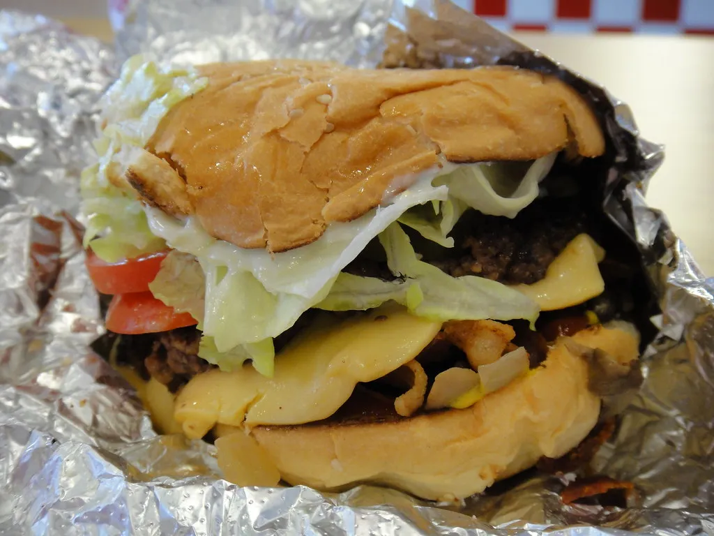 Five Guys bacon cheeseburger with lettuce, tomato, grilled onions and fried onions in its foil wrap