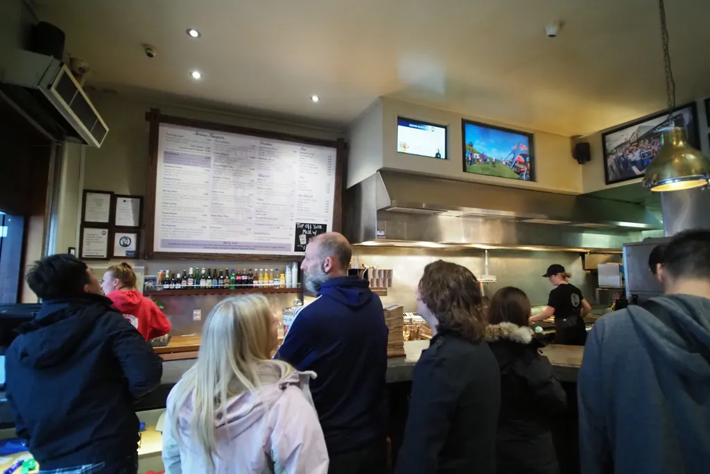Customers queuing at the Fergburger counter in Queenstown under the menu board, with staff at the grill