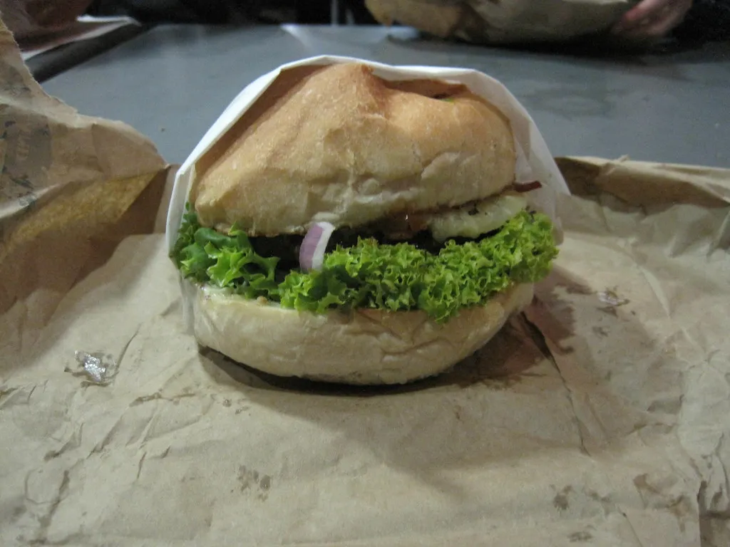 Fergburger beef burger on its paper wrapper with a tall soft bun, lettuce and red onion