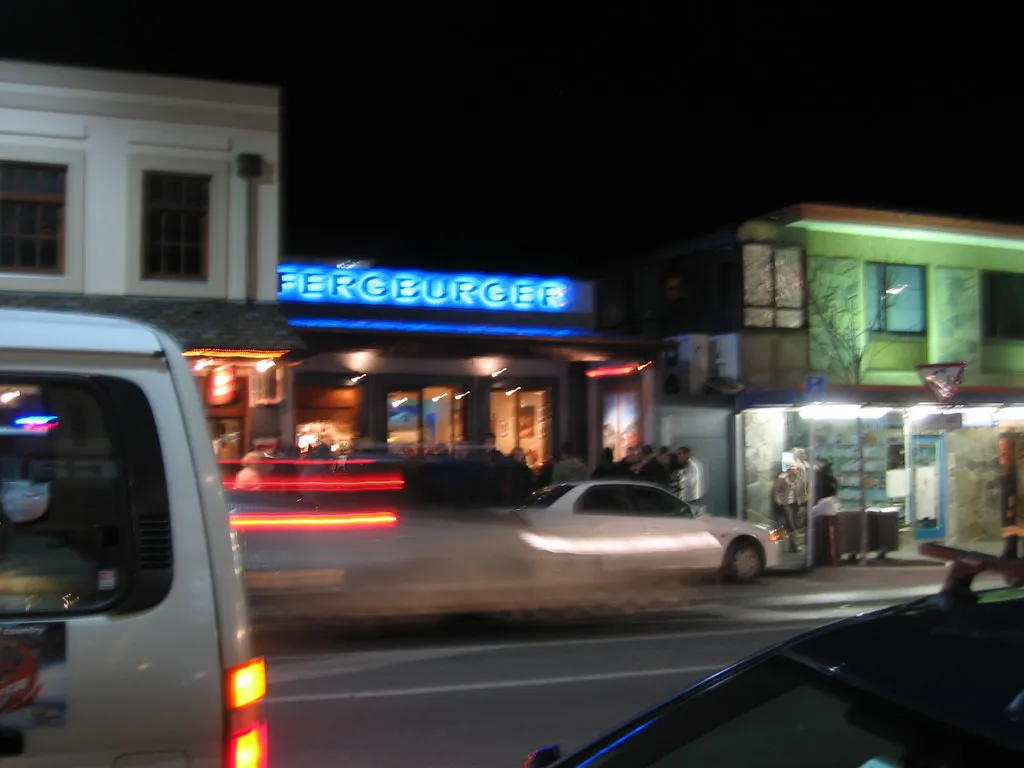 Fergburger neon sign lit up at night on Shotover Street, Queenstown, with late-night customers outside