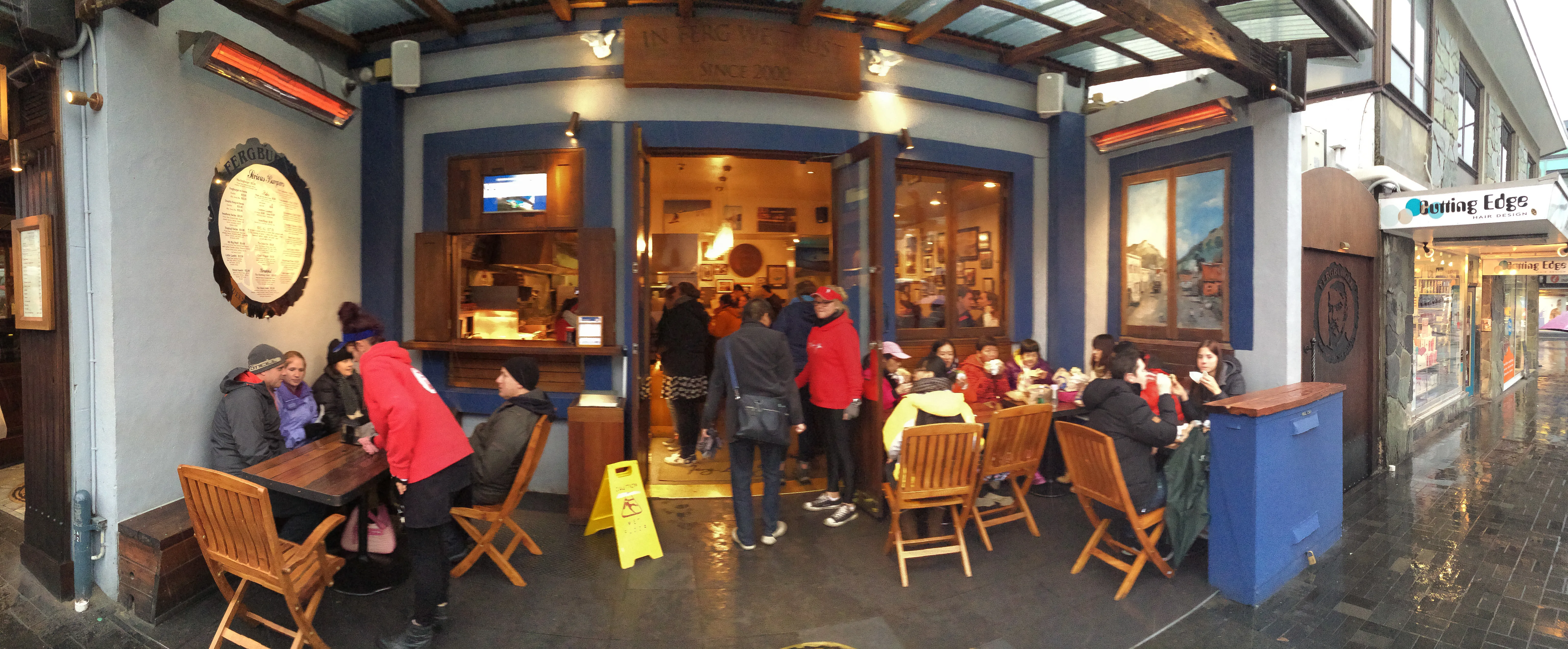 Fergburger terrace in Queenstown with the ‘In Ferg We Trust’ sign, round menu board and carved bearded Ferg face on the door
