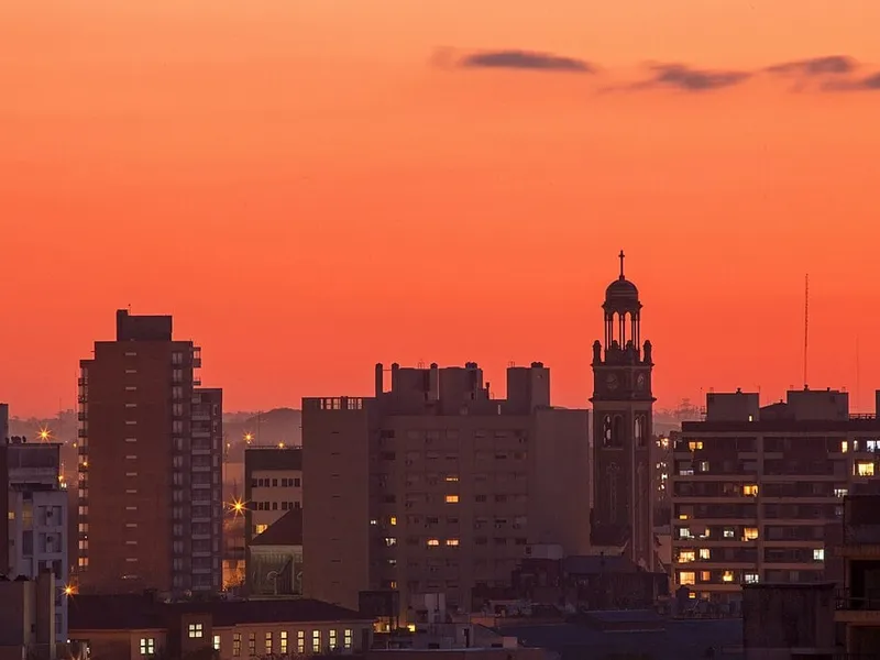 Rosario, en Argentine, au coucher du soleil : immeubles et clocher d'église sous un ciel orangé, dans la ville où Roses sert le meilleur burger de Rosario