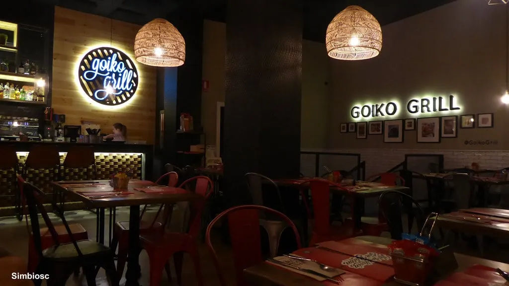 Interior de una hamburguesería Goiko con logo de neón, lámparas de mimbre y sillas metálicas rojas, el diseño de los comedores de Goiko Valencia