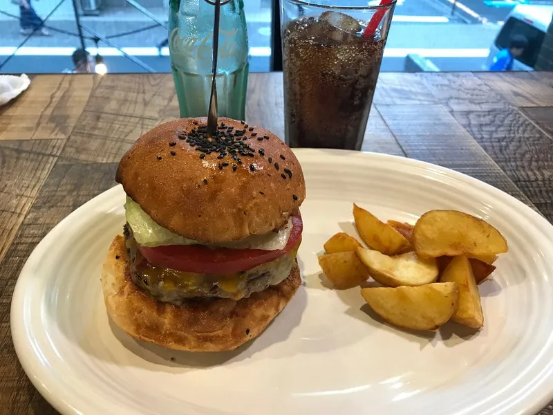 Cheeseburger du MUNCH'S Burger Shack à Tokyo, fromage fondu, tomate et salade dans un bun au sésame noir, servi avec des potatoes