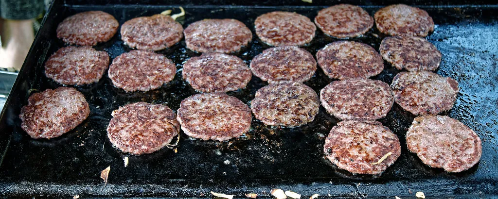 Burger patties cooking side by side on a flat-top griddle