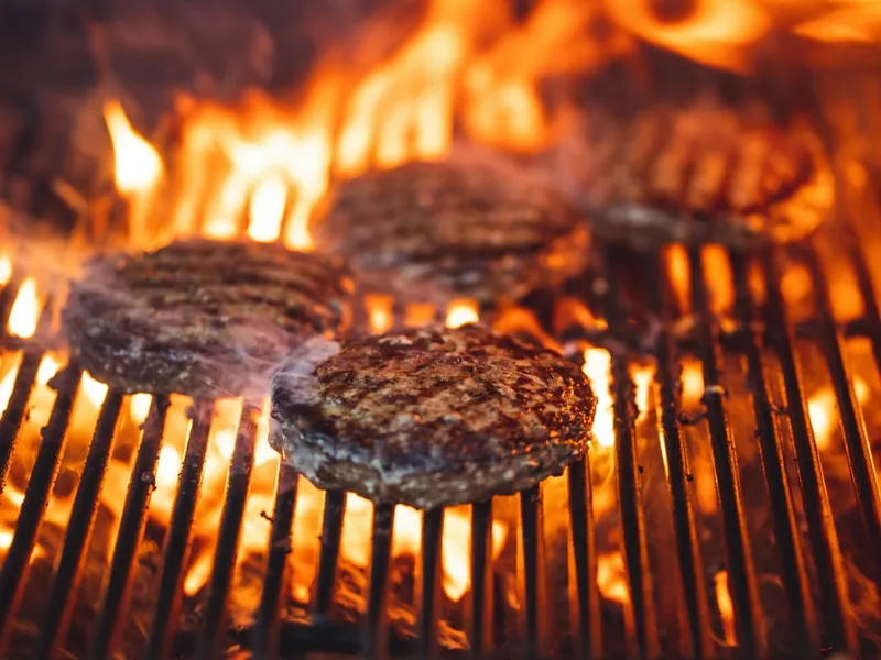 Steaks burger saisis au-dessus des flammes sur la grille d'un barbecue, croûte brune formée avant d'atteindre 71 °C à cœur